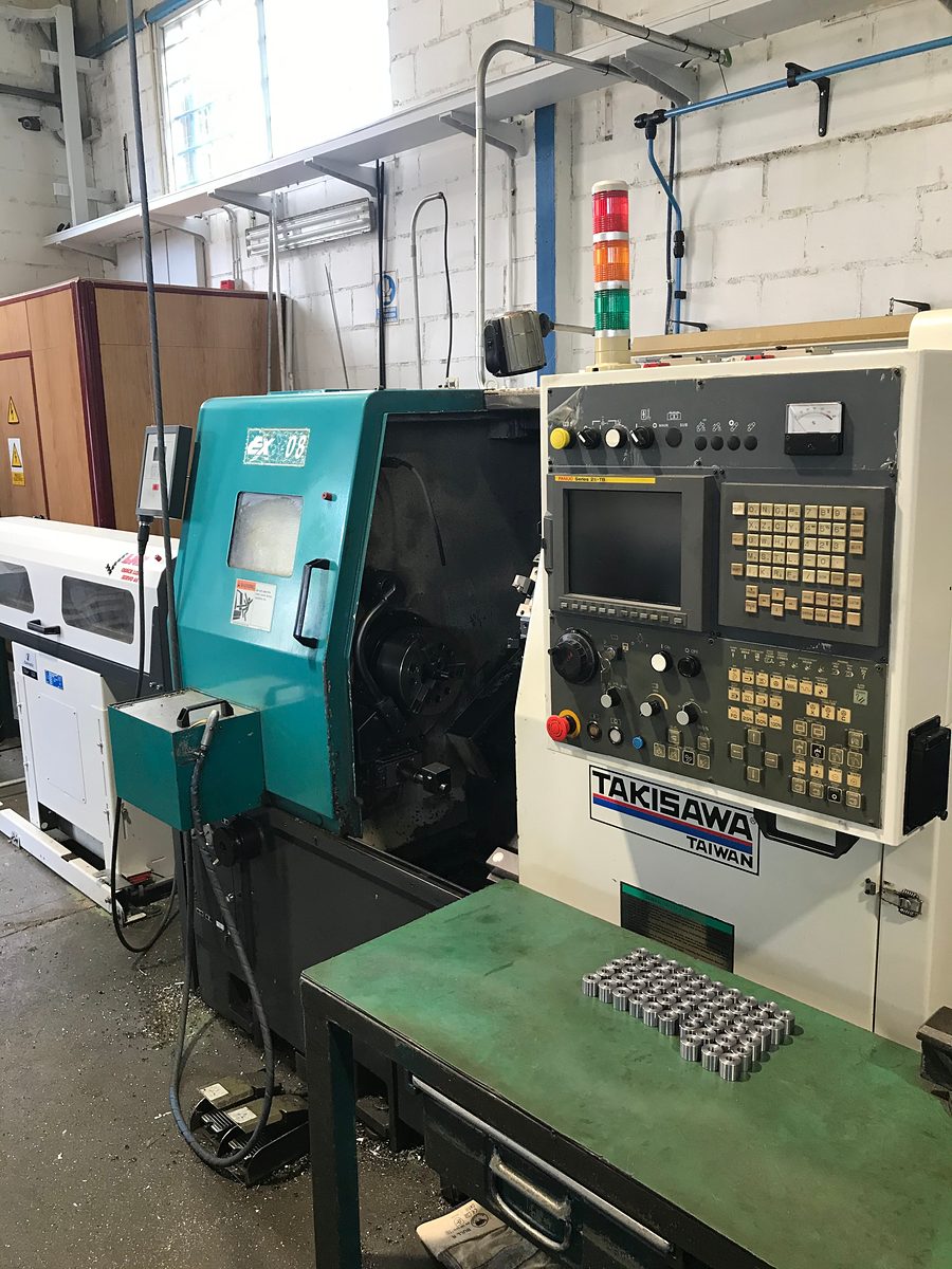 Torno CNC Takisawa con control Fanuc 21i-TB y piezas torneadas sobre la mesa